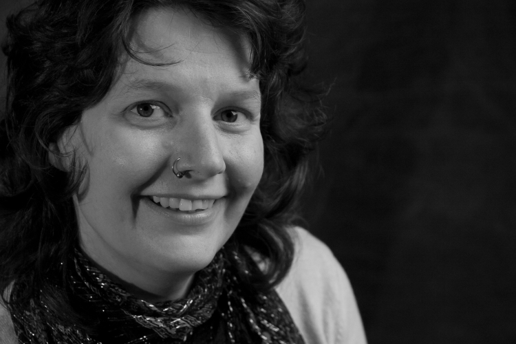 black and white headshot of Heidi Winters Vogel, a white woman with dark curly hair. Heidi is smiling warmly.